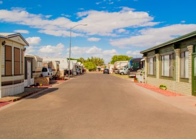 Photograph of the RV park grounds at Garden Oasis RV Resort. There's a paved road in the middle of the image, RV trailers can be seen on the left side of the street with the clubhouse to the right. Some cars are parked in the driveways of the RV sites.